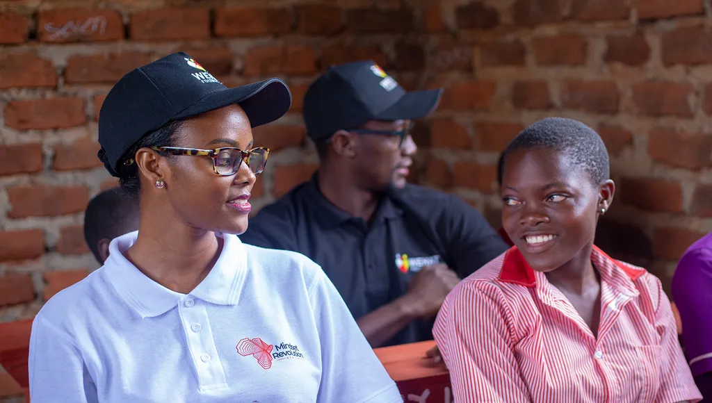 Girl child at school in eastern uganda sitting next to volunteer from mind project during WEHAT Foundation Uganda NGO visit to schools in eatern uganda 2023